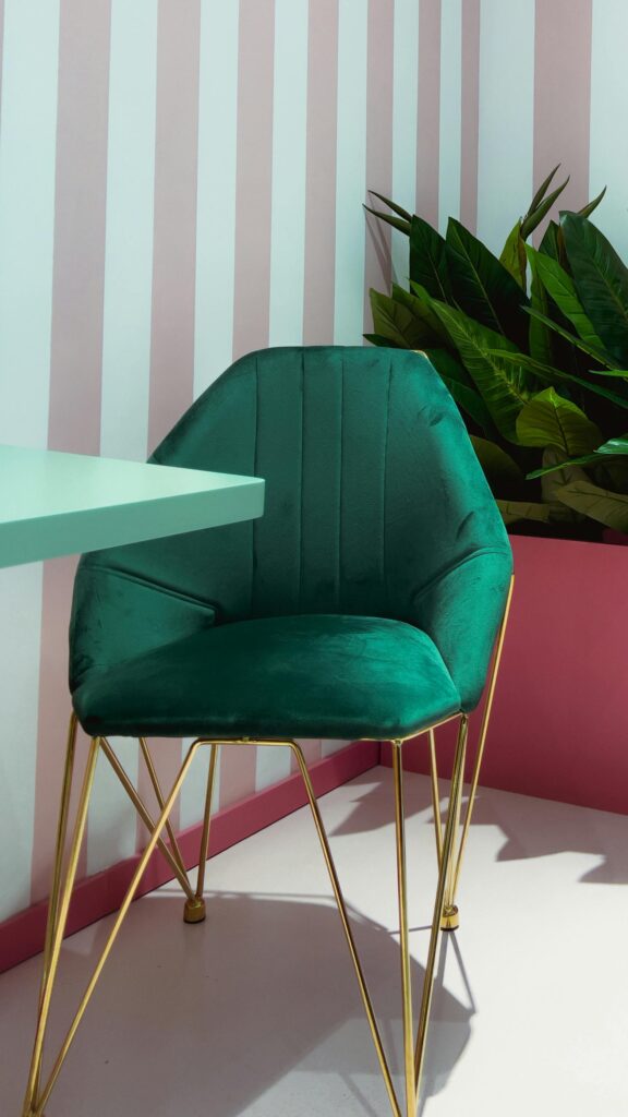 Sophisticated green velvet chair with gold legs in a chic interior setting enhanced by striped walls.